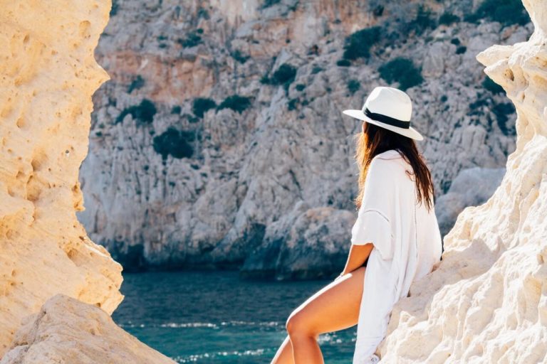 a person wearing a white hat and a white dress standing on a rocky cliff