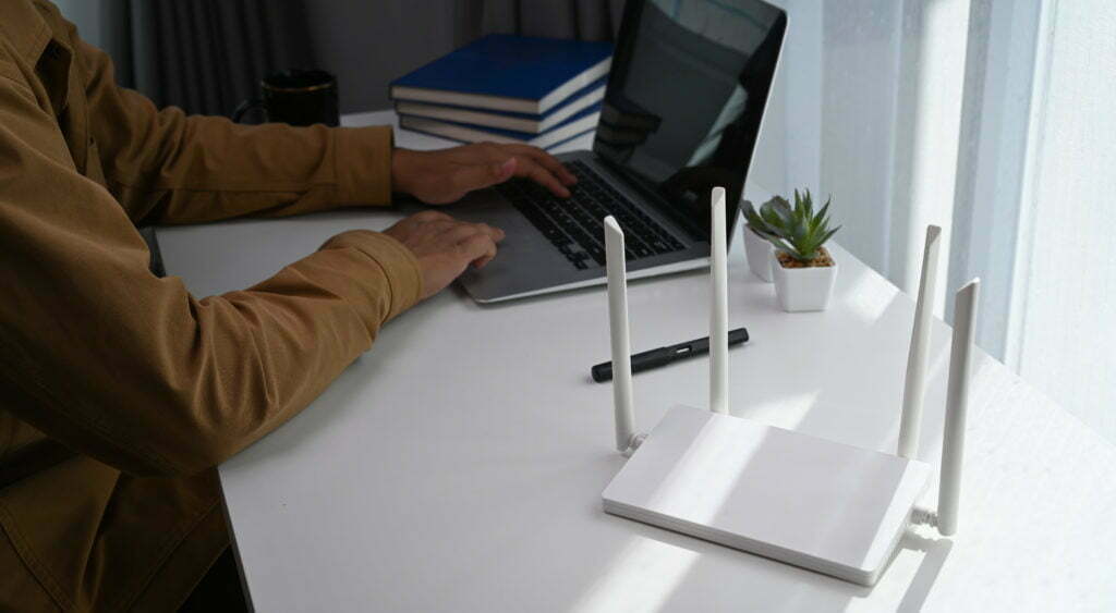 Young man working on computer laptop and sitting in front of high speed wireless internet router