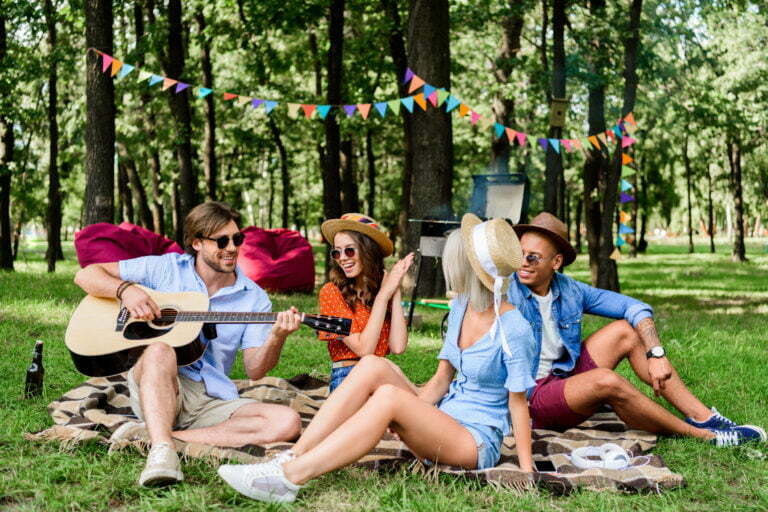 friends with guitar resting on blanket in summer park